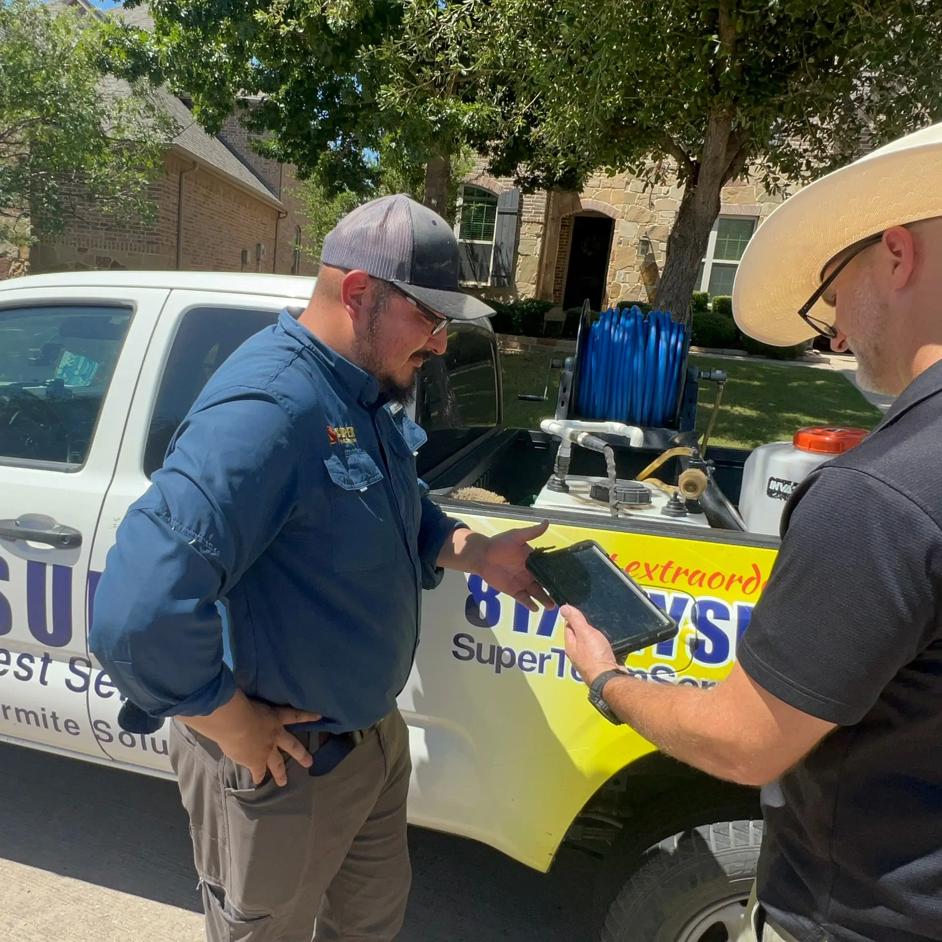 A Super Pest Services technician reviewing pest control details with a customer beside a branded service truck in a Dallas–Fort Worth neighborhood