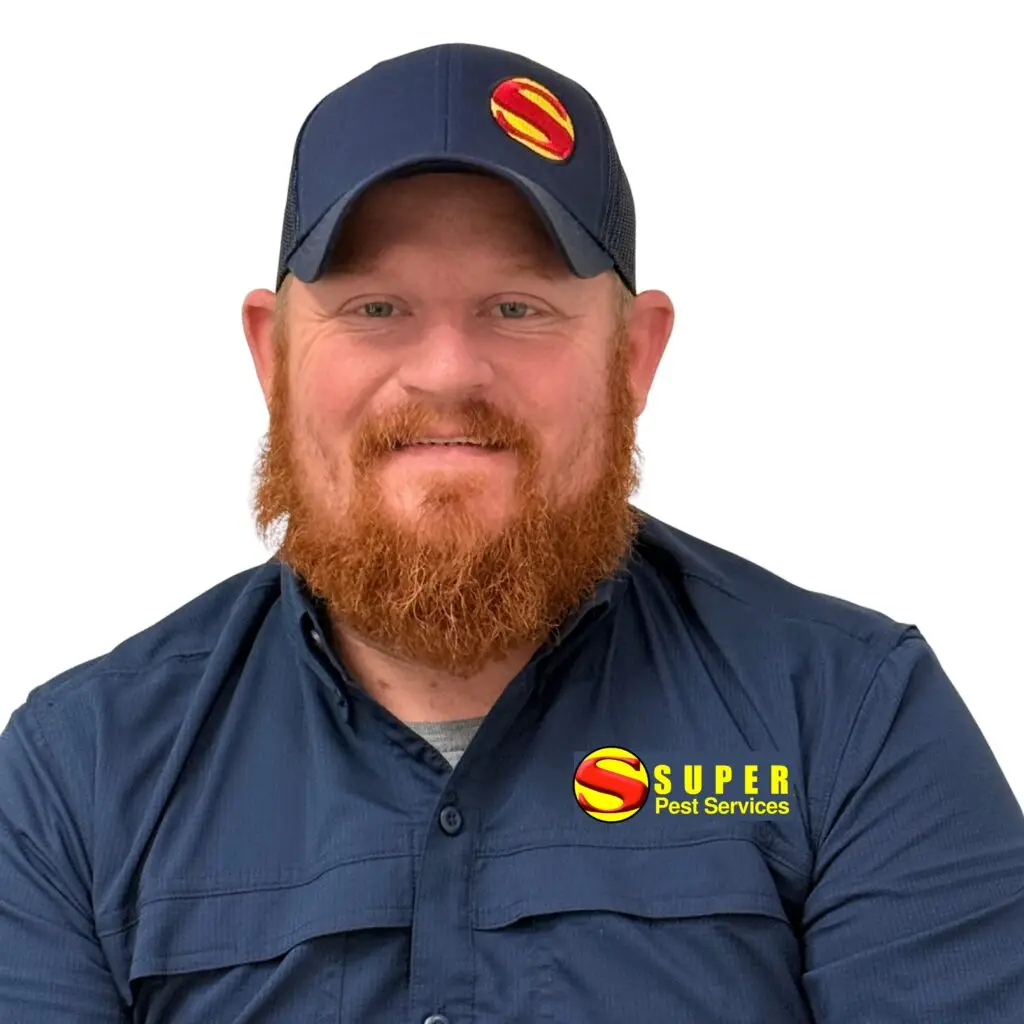 A smiling man with a red beard wears a navy blue cap and shirt, both featuring the Super Pest Services logo, against a plain white background.