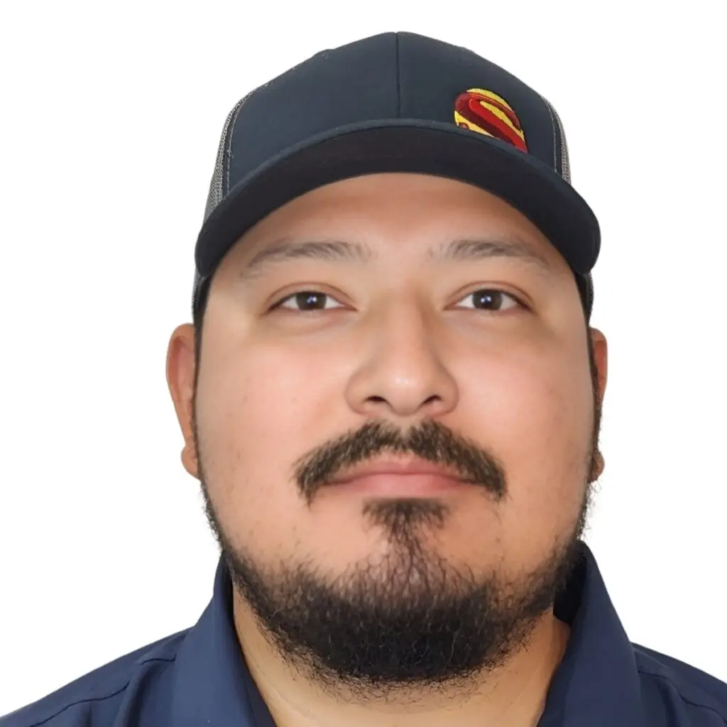 A man with a mustache and beard wearing a dark baseball cap with a red and yellow S logo and a dark collared shirt, looking at the camera against a white background.